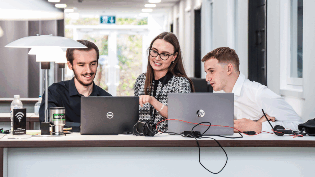Three people stood at a standing desk with laptops discussing commercial property management
